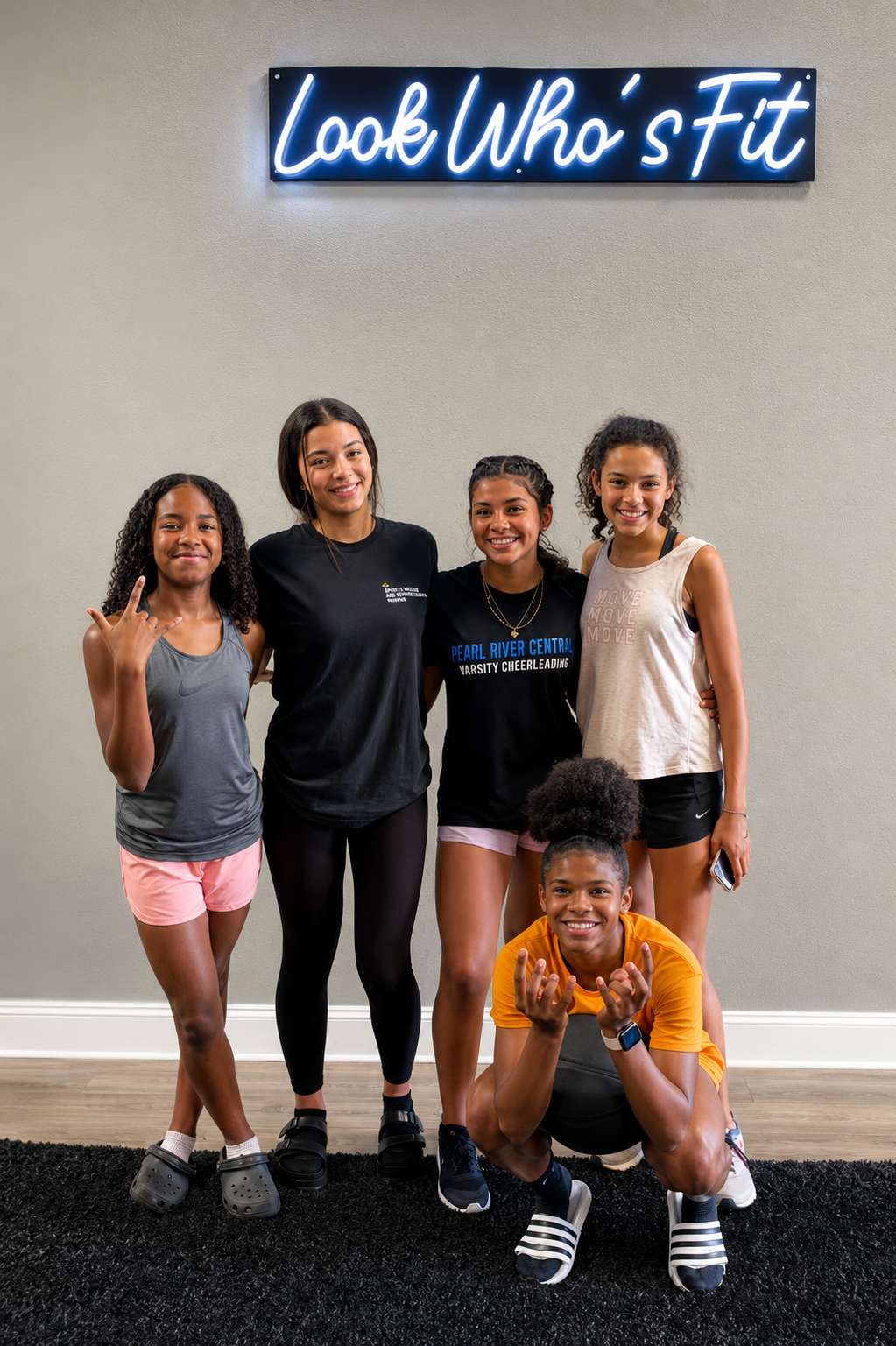 Group of young athletes smiling beneath the Look Who's Fit neon sign