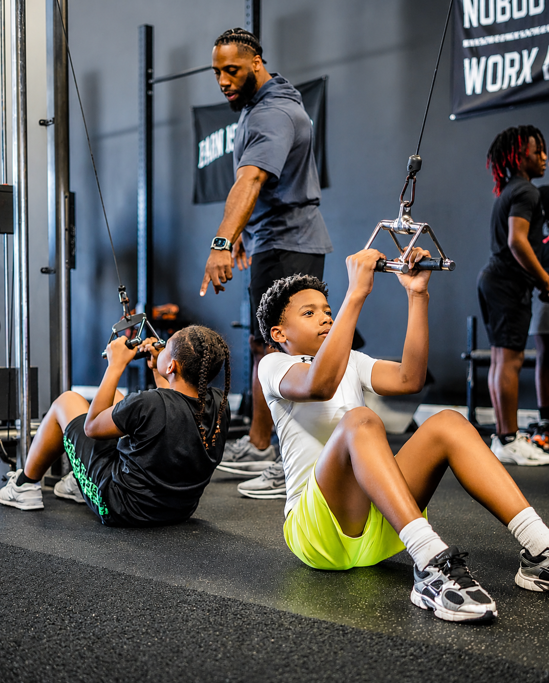 Coach guiding young athletes through a cable machine exercise