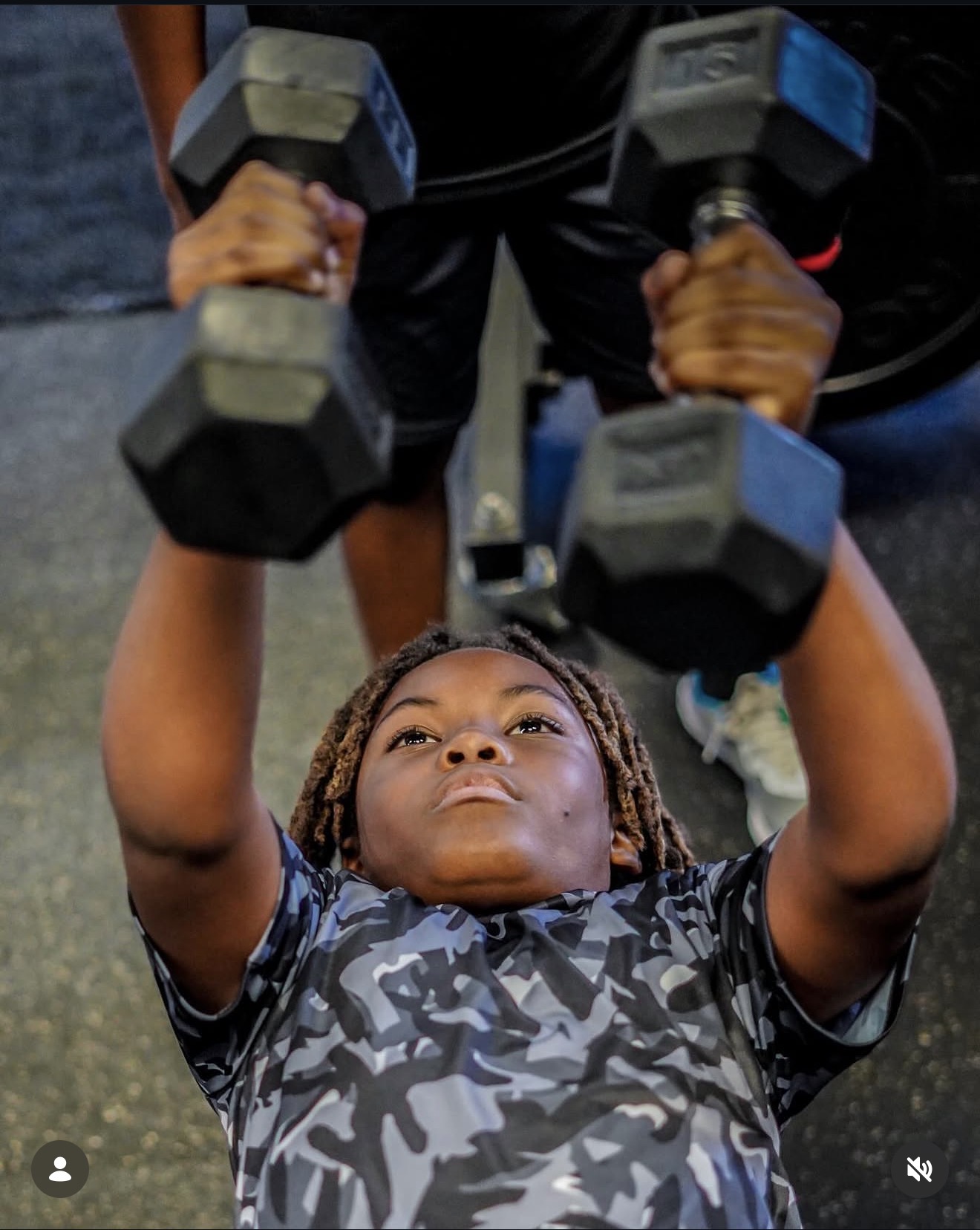Young athlete pressing dumbbells with a coach spotting overhead